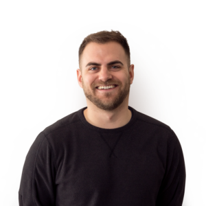 A man with short mousy brown hair a well groomed beard and wearing a black jumper